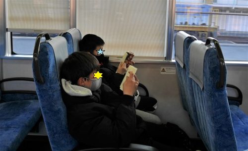 電車の中で読書をする小学生と中学生