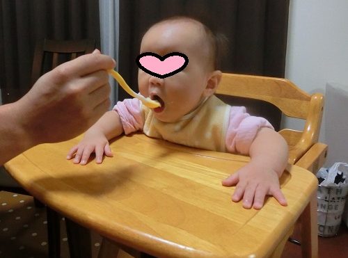 木製子供用椅子のベビーチェアで離乳食をあーんと食べている赤ちゃん
