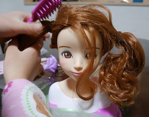 メガハウスのヘアメイクアーティストの人形の髪の毛を結んでいるところ