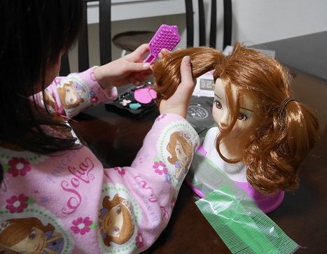 養生テープでテーブルにヘアメイクアーティストの人形を固定して遊ぶ女の子