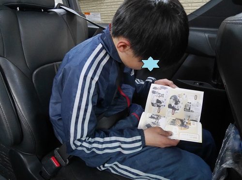 習い事の送迎の車の中で本を読む小学6年生の男の子