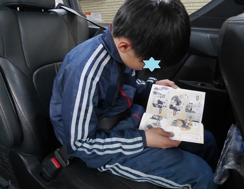 習い事の送迎の車の中で本を読む小学6年生の男の子