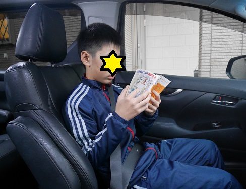 車の中で東野圭吾の「十字屋敷のピエロ」を読む小学校高学年男子